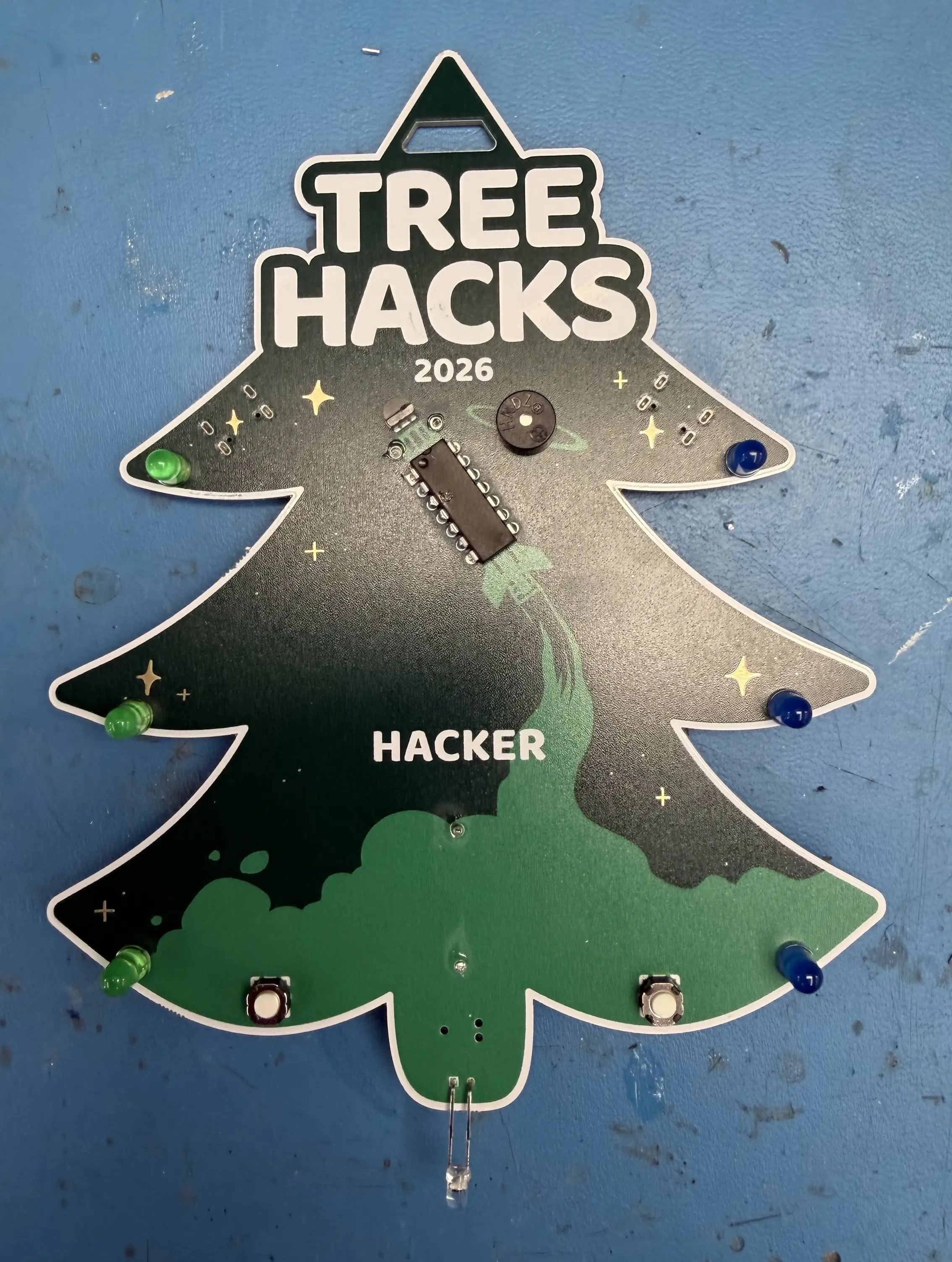 Front of a finished badge, with tree-shaped edge cuts, rocket artwork, and six LEDs