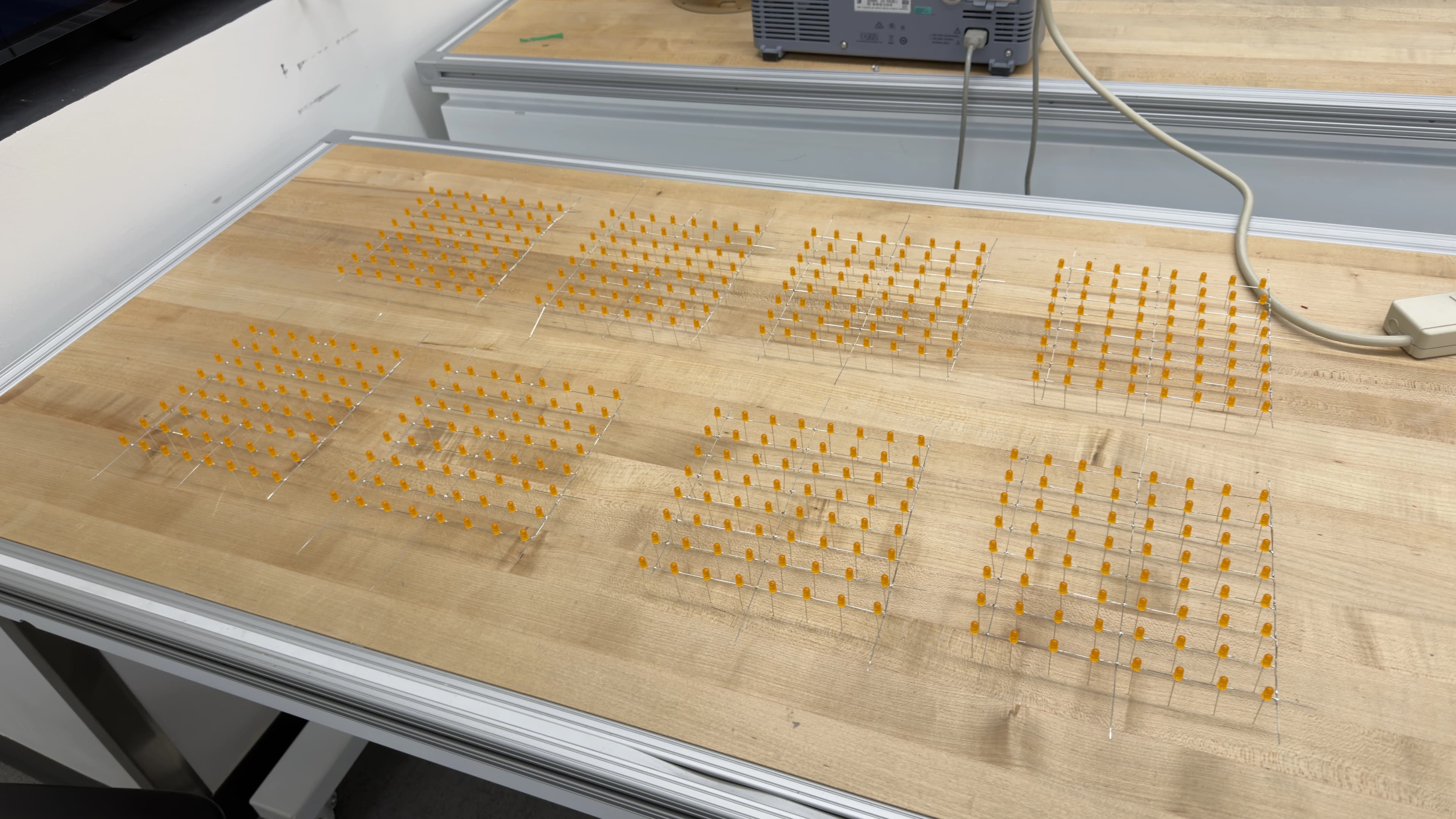 All eight completed 8x8 LED layers laid out flat on a wooden workbench